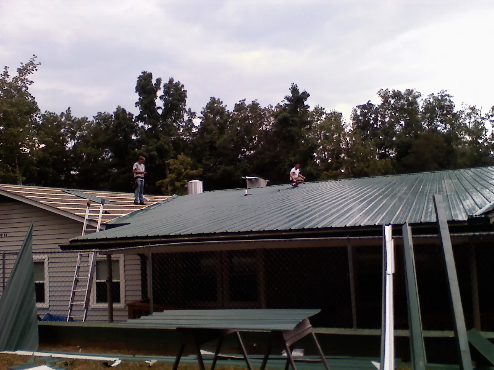 Two roofers installing green metal panels above a covered porch in Westmoreland